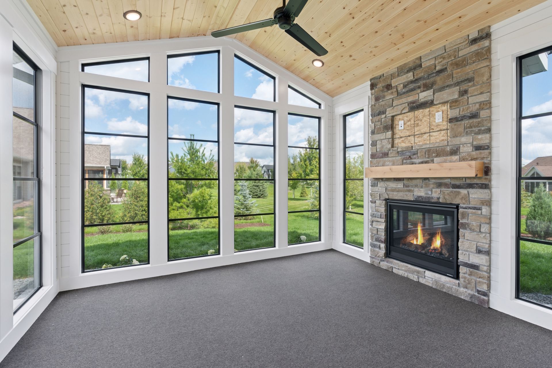 Cozy four-season porch with floor-to-ceiling windows and stone surround fireplace